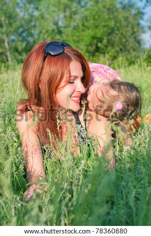 Kissing mother and baby daughter in grass on a meadow. Summer holiday.