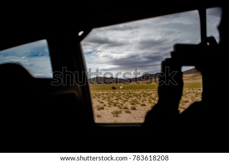 Tourist taking a picture with phone from 4x4 car window near Salvador Dali Desert during dessert crossing in Uyuni Salt Flats in Bolivia. 