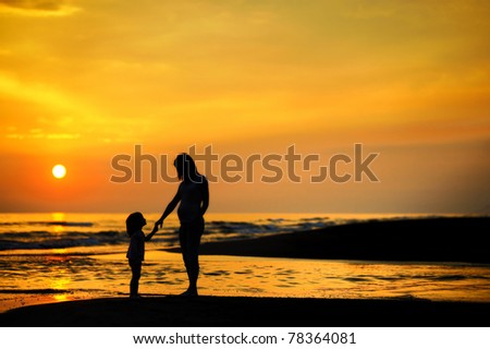 Pregnant mother and her child as silhouettes by the sea