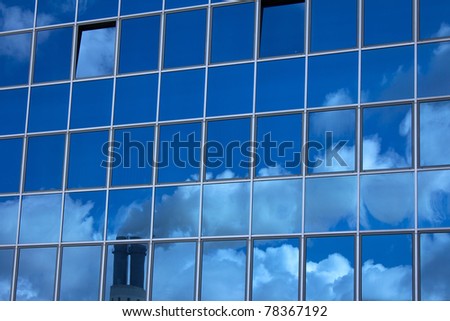 Glass facade with a reflection of a smoky chimney and clouds
