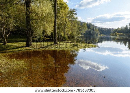 high water level in river Gauja, near Valmiera city in Latvia. summer trees surrounding and reflections of white clouds
