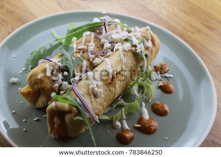 Delicious chicken burrito with salad, cheese, mayonnaise and ketchup on a white plate.