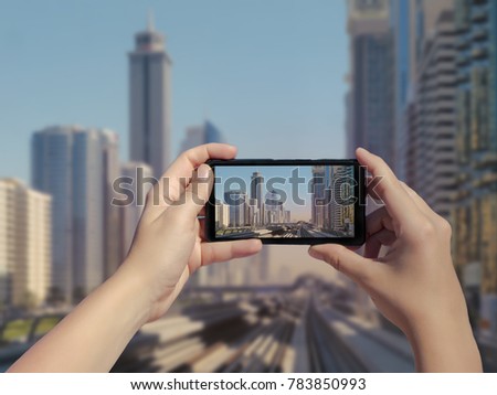 Female's hands take a picture of Dubai monorail and skyscrapers on mobile phone. Picture of subway road on downtown city Dubai on smartphone. United Arab Emirates