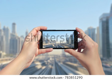 Female's hands take a picture of Dubai monorail and skyscrapers on mobile phone. Picture of subway road on downtown city Dubai on smartphone. United Arab Emirates 