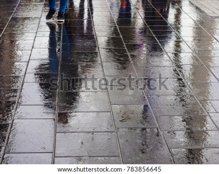 Reflection of people in wet pedestrian road in rainy cloudy weather.