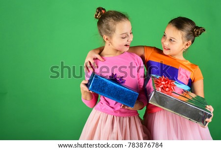 Birthday surprise concept. Sisters with wrapped gift boxes for holiday. Girls with curious smiling faces hug holding with presents on green background, copy space. Children open gifts for Christmas