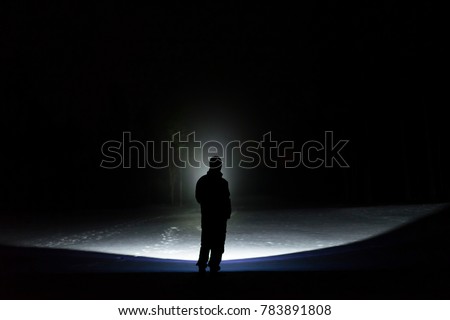 Man standing outdoor at night in forest shining forward with flashlight. Nice strong light beam. Beautiful abstract photo. Calm, peaceful and mystical image.