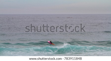 Girl surfer on pink surfboard paddling out for a surf