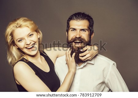 young couple of woman with pretty smiling face and blonde hair in black vest and handsome bearded man with long beard in white shirt in studio on grey background