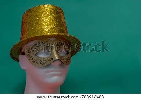 Gold top hat and mask on a green background.