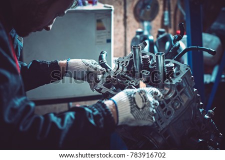 The young auto mechanic dismantles the opposing engine for diagnosis and repair at the stand in the workshop. Royalty-Free Stock Photo #783916702