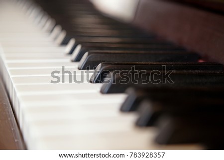 Close up of dusty old black and white piano keys on a brown wooden piano with selective focus and space for text. 