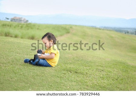 Little Asian toddler  playing change camera lens in the field with beautiful landscape background.