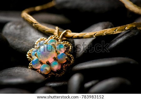 Opal pendant on serpentine gold chain resting on black pebbles.
