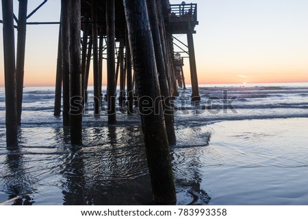 California Oceanside pier over the ocean at sunset with beach and surfers 