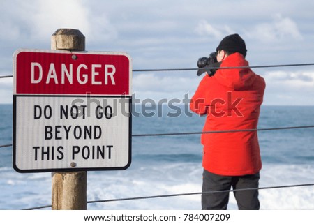 Photographer taking pictures beyond the Danger Point Sign. Taken in Pacific City, Oregon Coast, United States of America.