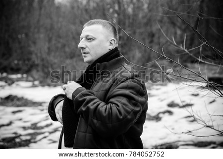 Portrait of a middle age man in warm clothing at forest on a cold day. Fashion handsome elegant man wearing black coat in winter day over trees forest background