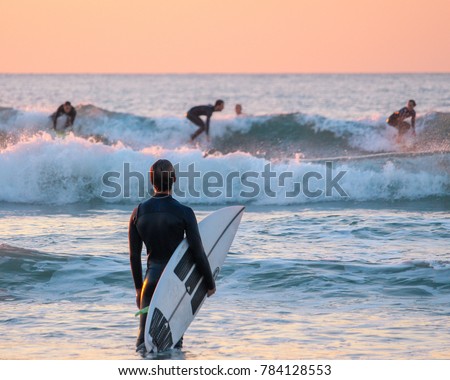Surfer watching his friends surfing from the shore  Royalty-Free Stock Photo #784128553