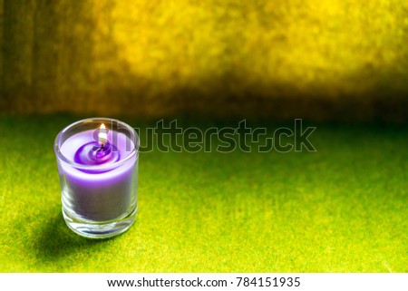 Glass cup with small purple candles. Put a candle on fire. Placed on a light green carpet. The back is a brown scene with natural light through. Leave it for the letter.