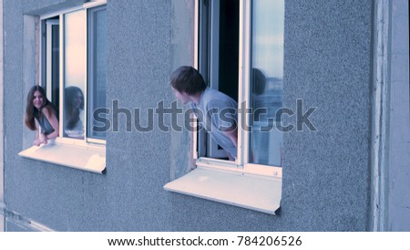 Neighbors talk to each other from the window. Young happy couple conversing in window. Neighbors concept. Young couple having a conversation while looking at each other over a window background Royalty-Free Stock Photo #784206526