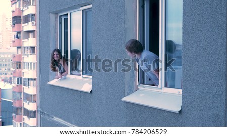 Neighbors talk to each other from the window. Young happy couple conversing in window. Neighbors concept. Young couple having a conversation while looking at each other over a window background Royalty-Free Stock Photo #784206529