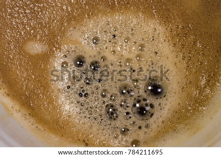 Fresh cup of Americano coffee seen close-up, showing the myriad of bubbles and thick froth. Part if the plan ceramic mug may be seen in this close-up image, taken in a well-known coffee franchise.