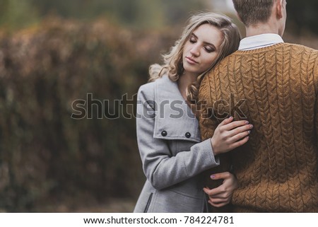 Young girl hugs guyâ??s back with blond hair, lady  show love, affection. Boy and girl of European appearance with warm clothes, pictures with soft background bokeh blur fall. Concept of happiness