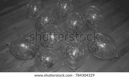 Black and White image of Balloons with Confetti Inside with a Wood Floor Background
