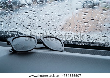 Sunglasses placed in front of the car and rain fell on the car window. Royalty-Free Stock Photo #784356607
