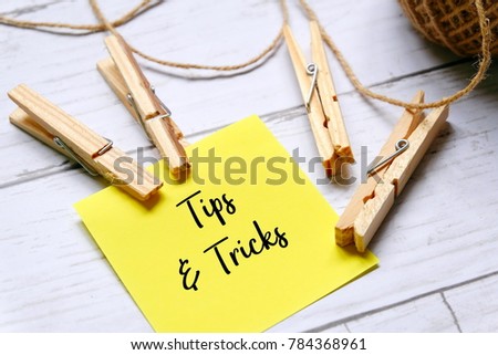 Yellow sticky notes written with TIPS AND TRICKS with cloth pegs and brown rope on white wooden background.