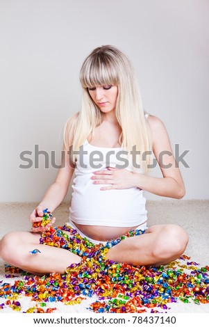 Young pregnant woman sitting among colorful candies