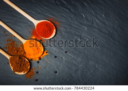 Spices in wooden spoons over black stone background, top view with copy space