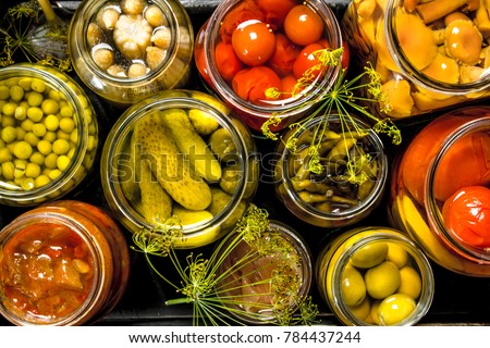 Preserves vegetables in glass jars in an old box. On the black chalkboard. Royalty-Free Stock Photo #784437244