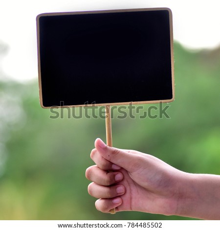 man holding an small blackboard ( chalk board) with green bokeh background.selective focus.