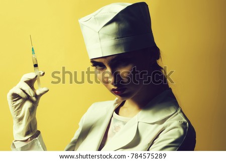 Beautiful young doctor in medical uniform holding syringe with liquid on yellow background