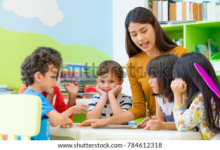 Asian female teacher teaching mixed race kids reading book in classroom,Kindergarten pre school concept Royalty-Free Stock Photo #784612318
