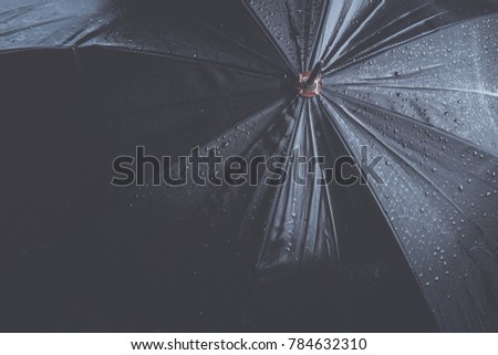 Raindrops falling on black umbrella outdoors.