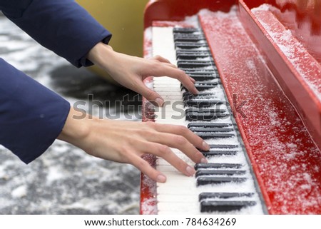 A young girl plays a red piano with keys covered in snow