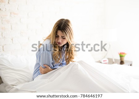 Young Caucasian woman in pajamas grabbing her belly while suffering from stomachache in her bed Royalty-Free Stock Photo #784646197