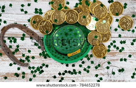 St Patrick good luck hat, green clovers and horseshoe with shiny gold coins on rustic white wooden boards 