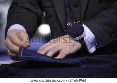 Dressmaker’s hands marking fabric cloth on a tailor cutting table. 