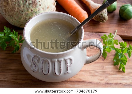 Bone broth made from chicken in a soup bowl on a wooden table, with vegetables in the background
