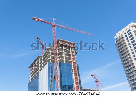 Working crane on a modern glass office building under construction against cloud blue sky in downtown Dallas, Texas, USA. Urban development and construction concept. Industrial background.