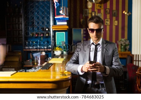 Young businessman using smartphone in a barand wearing sunglasses