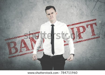 Caucasian businessman showing his empty pocket pants while standing with word of bankrupt in the background