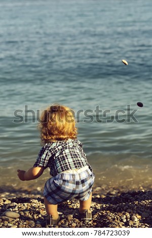 Baby boy in blue checkered shirt standing with back looking on horizon on beach of ocean or sea water sunny day outdoor on natural background, vertical picture