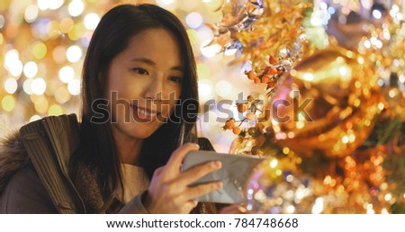 Woman taking photo on cellphone on Christmas tree decoration at night 