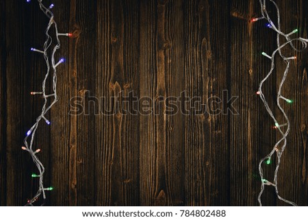 Fancy blinker light bulbs or garlands and wreath on wood table for Christmas or New years decoration background, space for add text or picture.