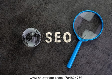 Alphabet abbreviation SEO and globe with blue magnifying glass on dark cement background using as SEO Search engine optimization concept.