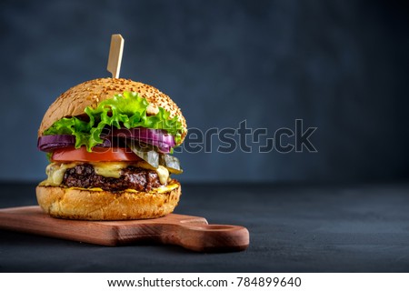 Tasty grilled beef burger with lettuce, cheese and onion served on cutting board on a black wooden table, with copyspace Royalty-Free Stock Photo #784899640